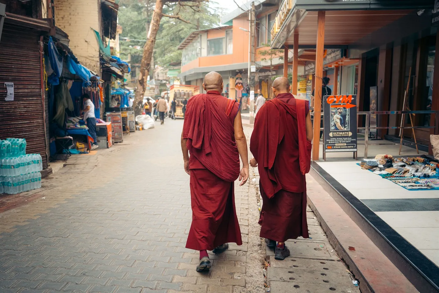 Two monks in red robes walking down a street of shops in McLeod Ganj